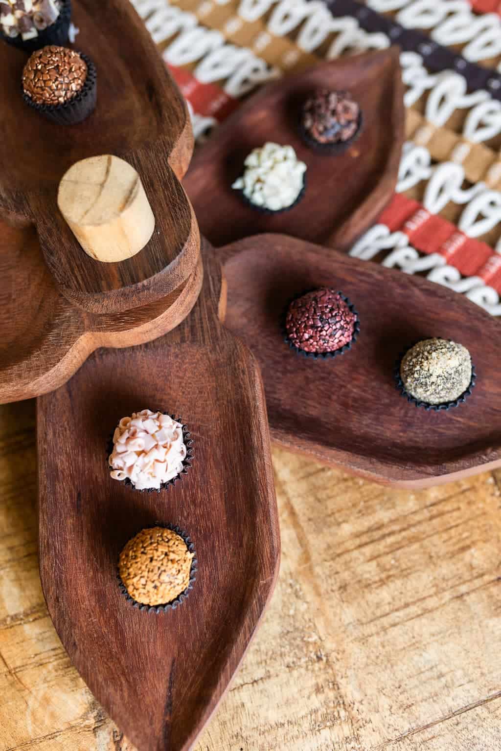 450A6344 Six assorted chocolate truffles are displayed on a rustic wooden platter with a patterned tablecloth in the background—an elegant choice for corporate gifts from Durham or Morrisville.
