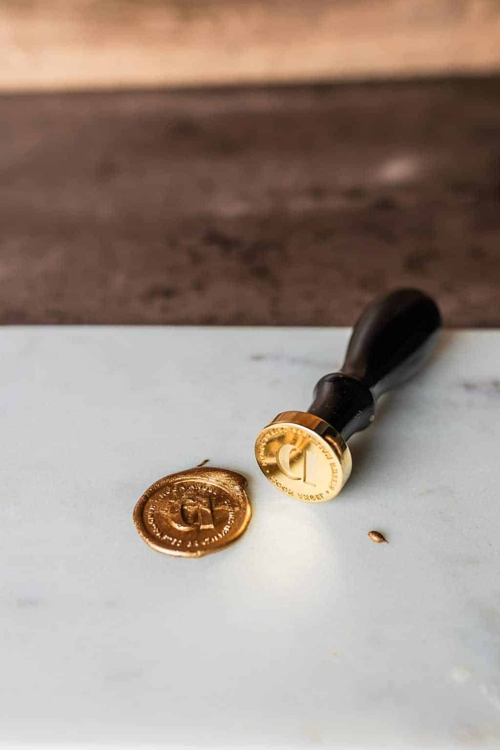 A gold wax seal stamp with a black handle, perfect for Corporate Gifts, is placed next to a freshly stamped gold wax seal on a white surface.