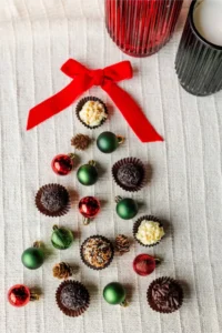 The 8 piece Holiday Gift Box is artfully displayed in the shape of a Christmas tree, adorned with small ornaments and topped with a red bow on a white textured background.